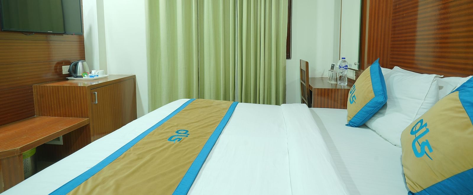 Side view of a deluxe room featuring a king size bed, a television, and a window covered by curtains at DLS Hotels The Rock Castle.